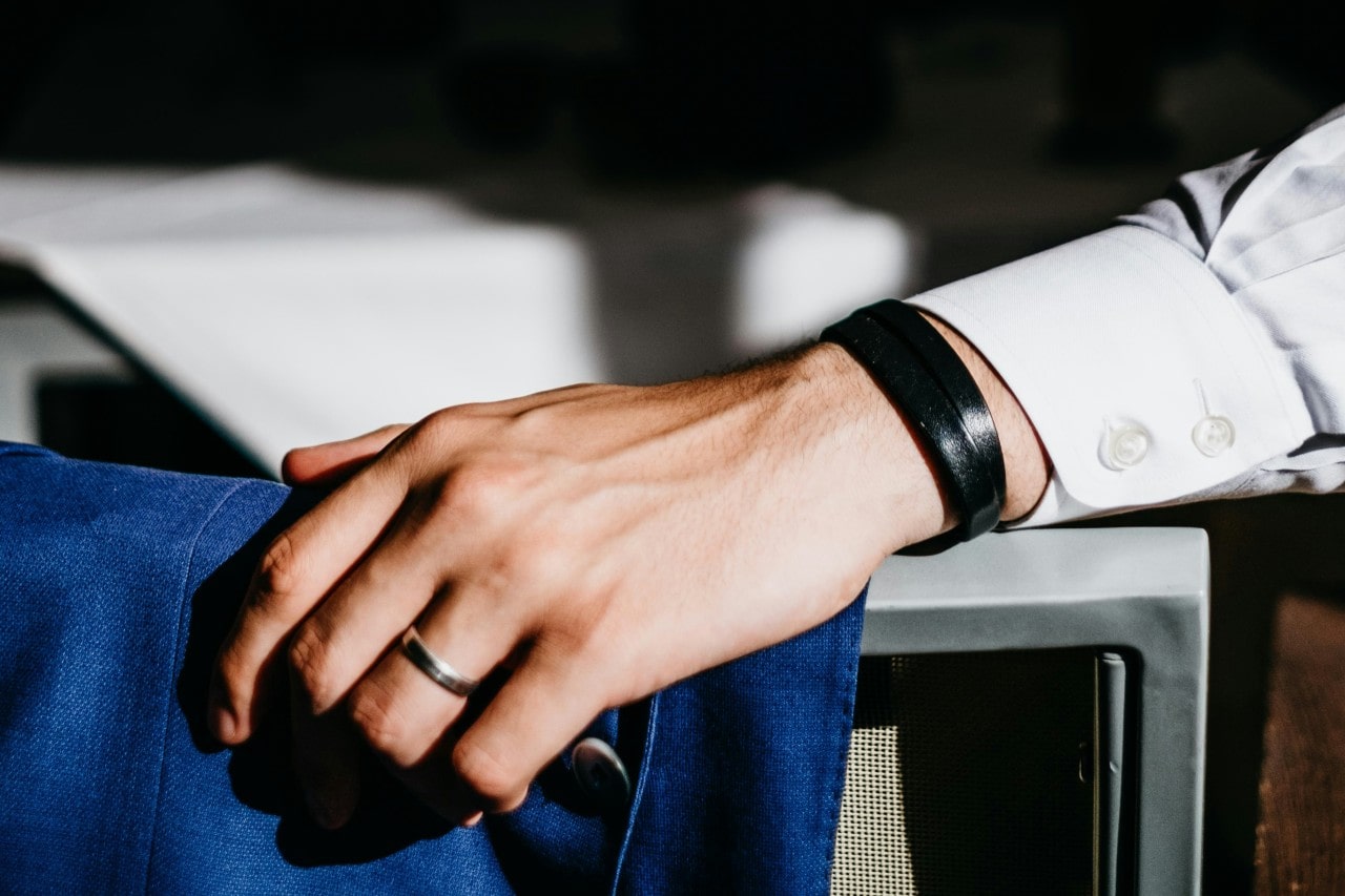 a man resting his hand on the back of a chair wearing a metal wedding band