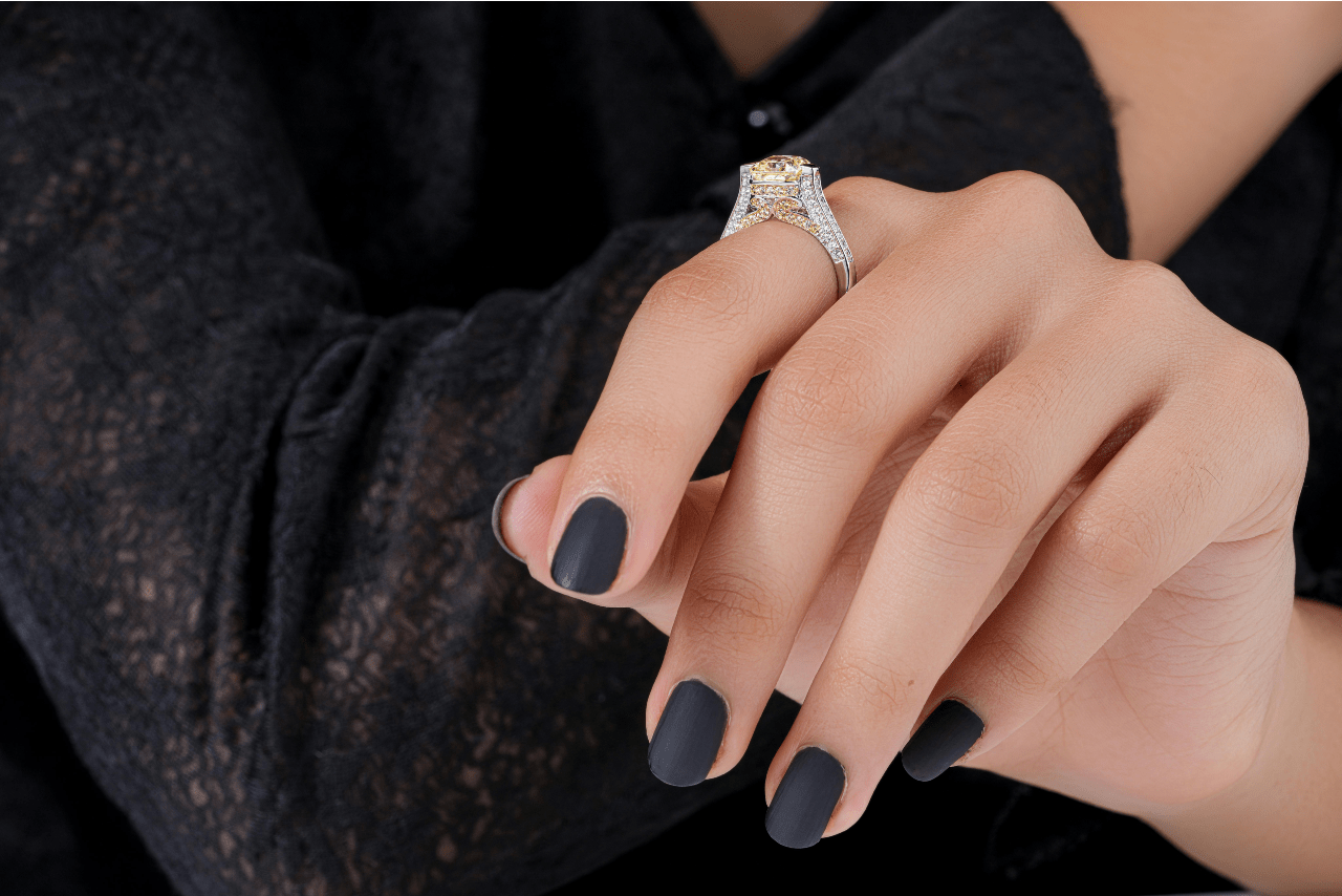 a woman’s hand with black nails and an elaborate diamond engagement ring