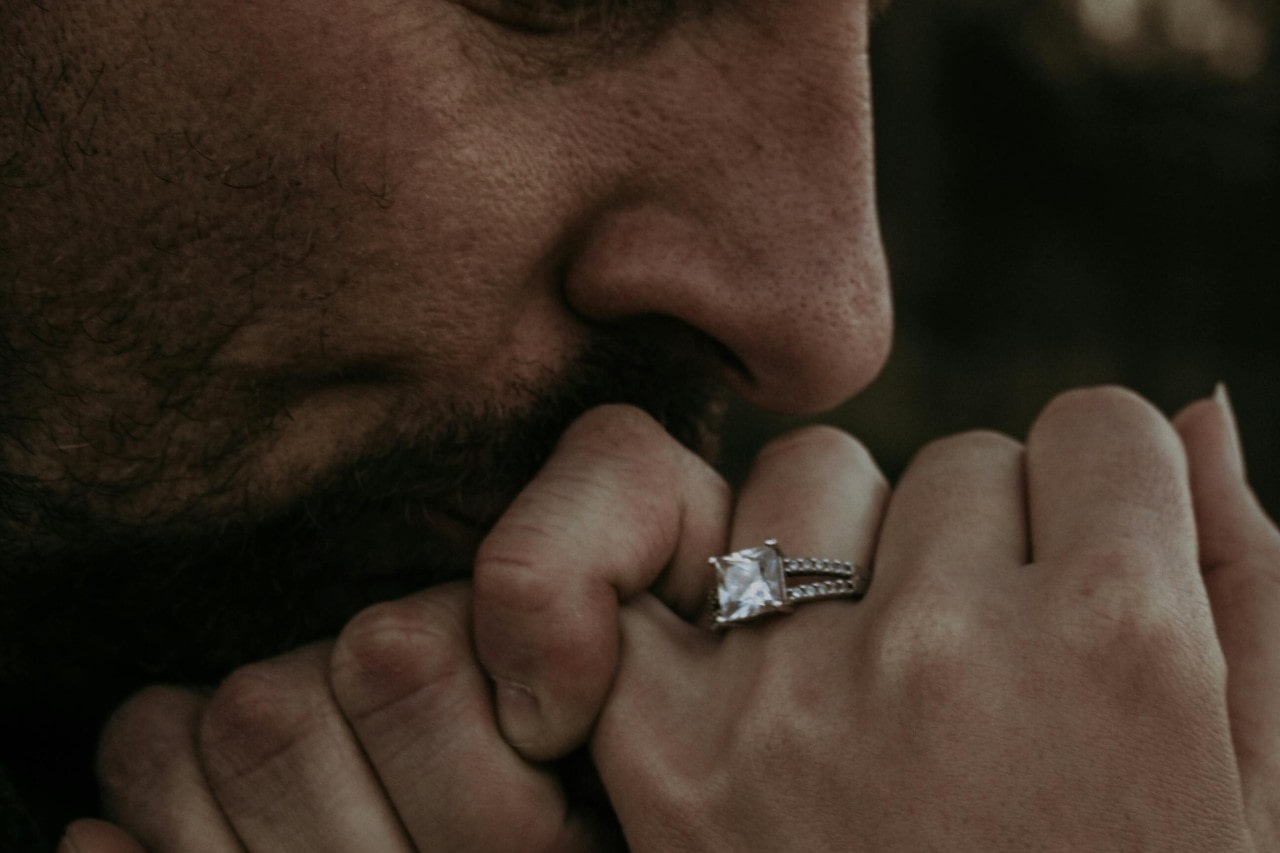a man kissing a woman’s hand wearing an engagement ring
