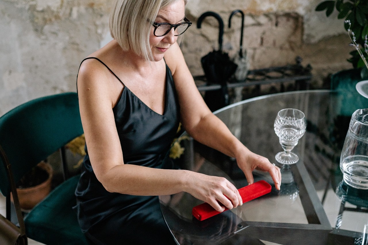 a woman at glass table opening a red necklace box a woman at glass table opening a red necklace box