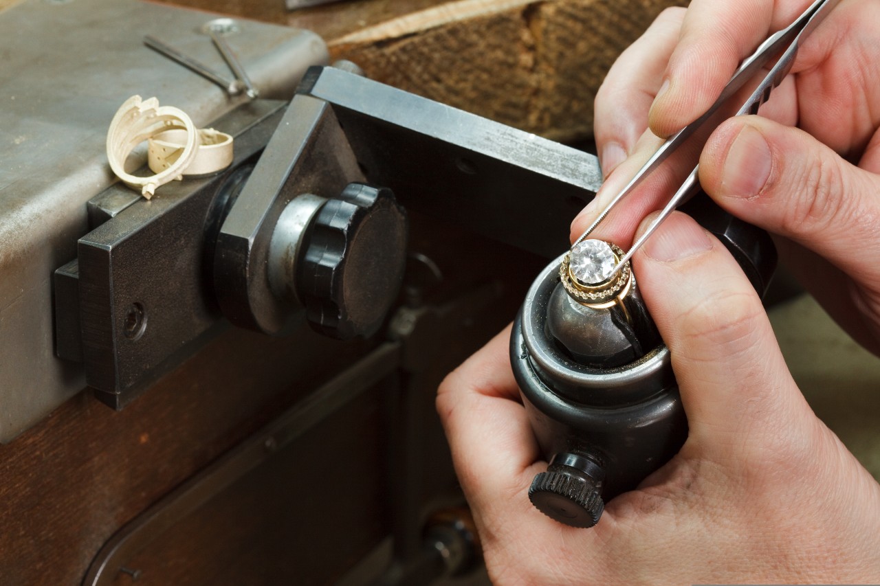 A jeweler sets a large diamond into a vintage piece of jewelry. A jeweler sets a large diamond into a vintage piece of jewelry.