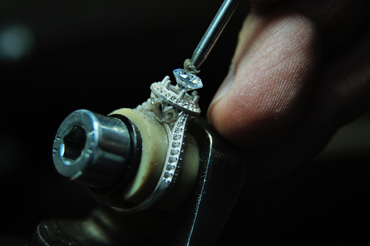A jeweler sets a diamond in a ring setting in a dark workshop. A jeweler sets a diamond in a ring setting in a dark workshop.