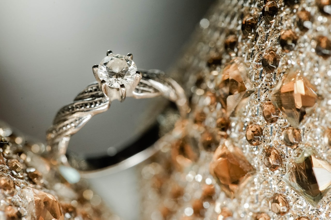 A close-up of a vintage-style engagement ring displayed in lavishly beaded fabric.