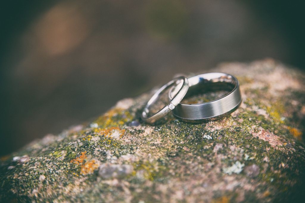 A close-up of two simple yet elegant wedding bands displayed one on top of the other on a lichen-covered stone.