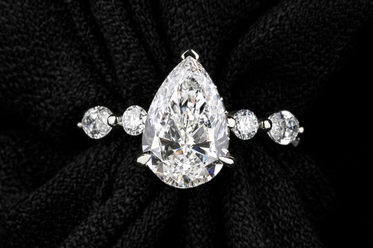 A close-up of a distinctive engagement ring with a pear center stone and large diamonds along the band.