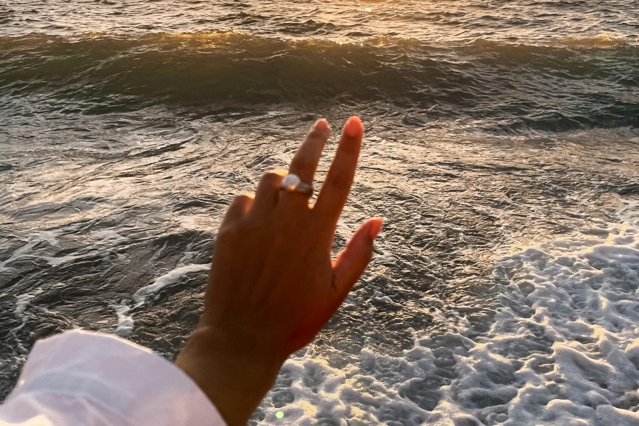 a woman’s hand outstretched towards the ocean, wearing a gold gemstone fashion ring a woman’s hand outstretched towards the ocean, wearing a gold gemstone fashion ring