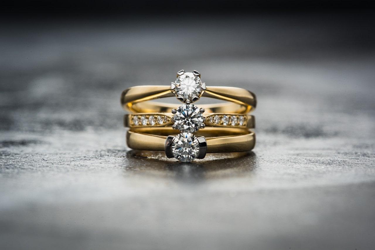 three yellow gold engagement rings sit on top of each other on a black background. three yellow gold engagement rings sit on top of each other on a black background.