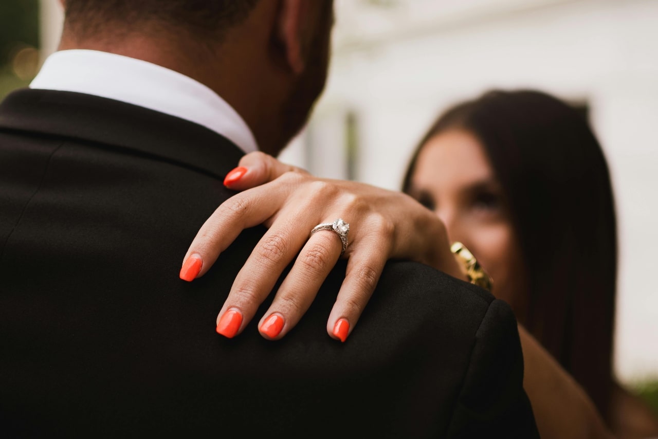 A bride’s hand resting on her groom’s shoulder, a white gold engagement ring on her finger. A bride’s hand resting on her groom’s shoulder, a white gold engagement ring on her finger.