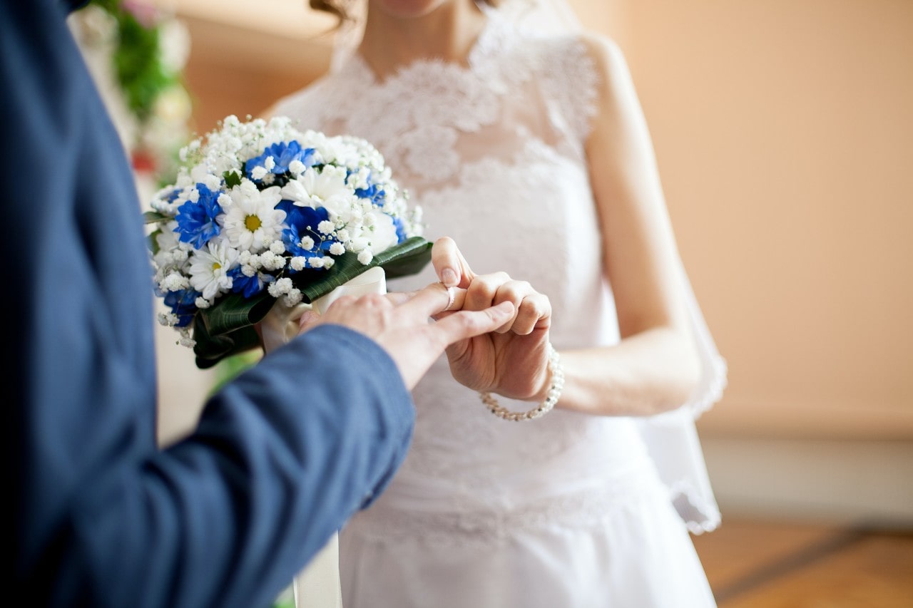 a bride placing a wedding band on her grooms finger at the altar a bride placing a wedding band on her grooms finger at the altar